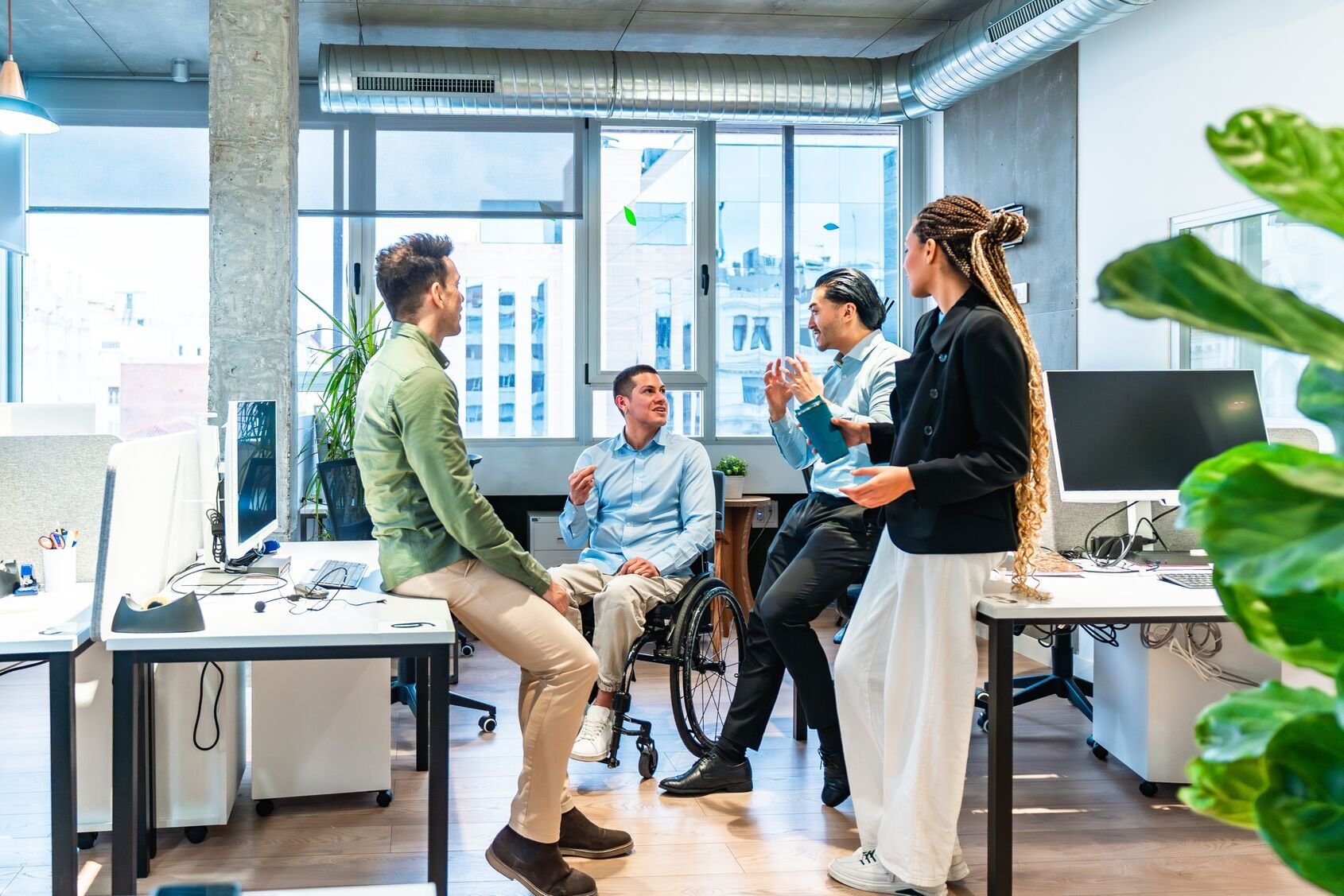 Web_Wide - Įvairialypė verslo komanda aptaria projektą moderniame biure su neįgaliu kolega vežimėlyje